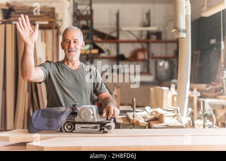 Smiling worker waving with a hand sander machine Stock Photo