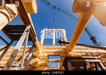 Worker carpenter builder working on roof house of log structure background blue sky. Stock Photo