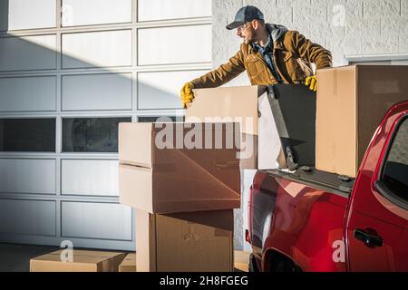 Caucasian Men in His 40s and Large Moving Boxes Delivery Using Pickup Truck. Commercial Gate Unloading. Stock Photo