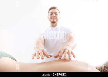 Doctor opens patient chakras with power of energy, reads aura. Closeup of hands on background of woman back. Stock Photo