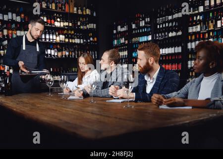 Sommelier pours red wine into glass from decanter to evaluate taste, tasting for friends in restaurant. Stock Photo