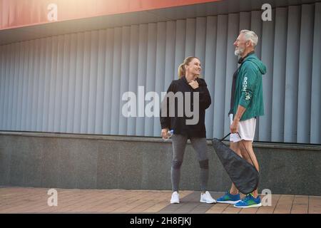 Cheerful middle aged sportspeople, man and woman in sportswear talking while standing together outdoors ready for workout Stock Photo