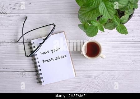 Notepad with text, New Year Fresh Start, with coffee, eyeglasses and green plant on table. Top view. Stock Photo