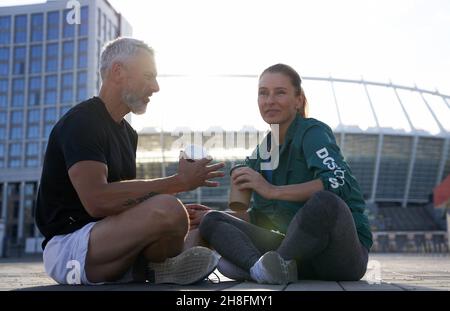 Sportive fit couple having conversation while sitting outdoors after morning workout on a sunny summer day Stock Photo