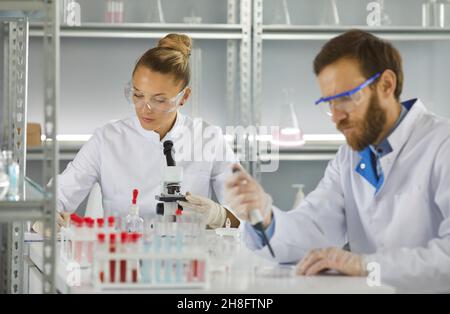 Scientists in the lab studies microorganisms under a microscope by taking a sample with a pipette. Stock Photo