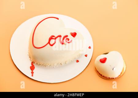 Mousse Heart shaped cake with the inscription love and small cupcake in the shape of heart on orange background for Valentine's Day and February 14th Stock Photo