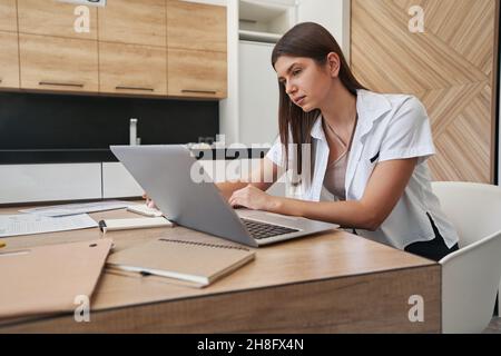 Focused calm woman sitting at laptop indoors Stock Photo