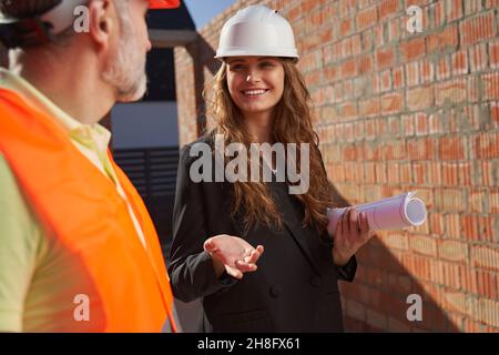 Aspiring woman in hardhat talking to contractor at building site Stock Photo