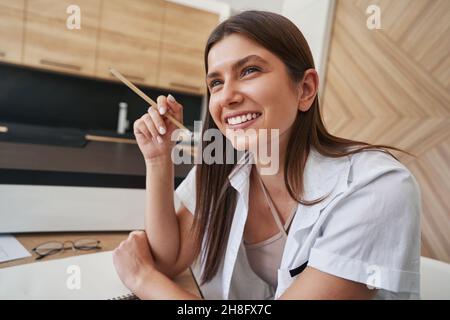 Joyous long-haired lady seated at table in room Stock Photo