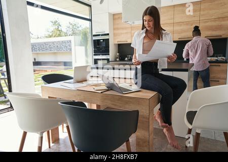 Focused barefoot woman with papers looking at her laptop Stock Photo