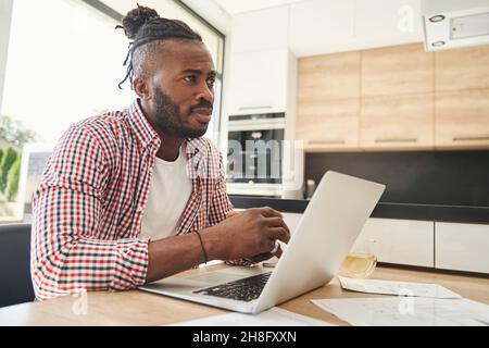 Upset guy sitting at his laptop in kitchen Stock Photo