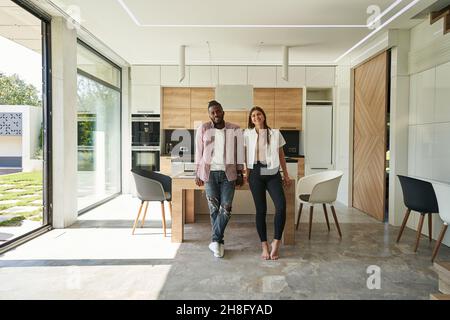 Joyous mixed-race couple posing for camera in kitchen Stock Photo