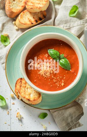 Hot tomato soup with toasts and basil. Soup with parmesan Red tomato soup in blue pottery. Stock Photo