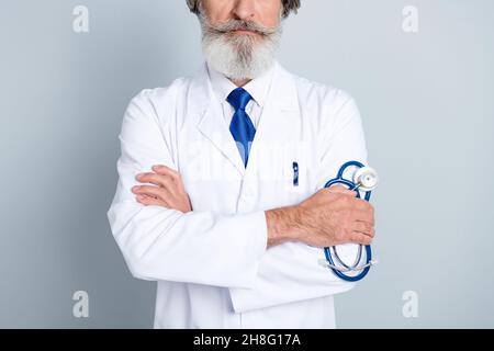 Cropped photo of mature doctor in coat holding stethoscope in his hand confident surgeon lab isolated over grey color background Stock Photo