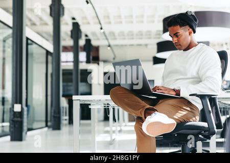 Focused software developer working on a new project. Young businessman using a laptop while sitting in a modern workplace. Creative businessman workin Stock Photo
