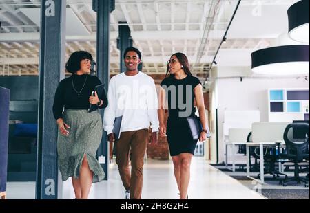 businesspeople on the move. Group of three confident businesspeople talking to each other while walking together in a modern office. Colleagues workin Stock Photo