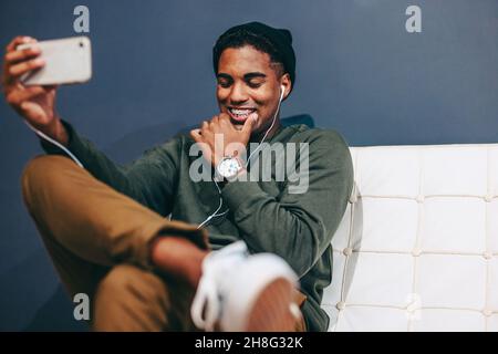 Happy young businessman taking a selfie in an office lobby. Young businessman smiling cheerfully while capturing a picture using a smartphone. Busines Stock Photo