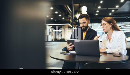 Two young entrepreneurs using a digital tablet while having a discussion in a modern workspace. Two young businesspeople using wireless technology whi Stock Photo