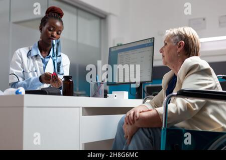 Therapist doctor showing lungs radiography to sick senior woman in wheelchair discussing recovery treatment. Therapist medic explaining disease expertise during medical consultation in hospital office Stock Photo