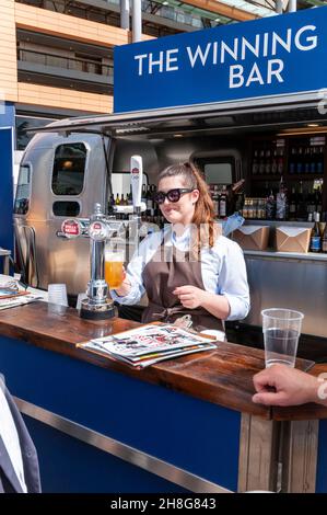 The Winning Post Bar at Royal Ascot racecourse, Berkshire, UK. Barmaid serving a customer with a draught pint of lager. Serving alcohol on sunny day