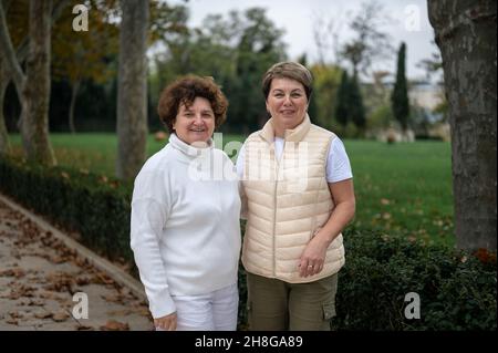Two older women standing outside and looking at camera. two middle-aged women walking in park autumn cool weather Stock Photo