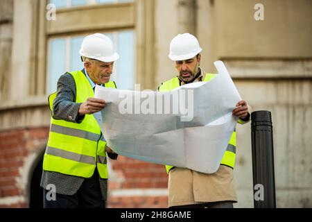 Two construction workers are looking at the plans on the paper Stock Photo