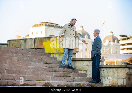 Two amazing senior businessmen are talking while smiling on the stairs Stock Photo