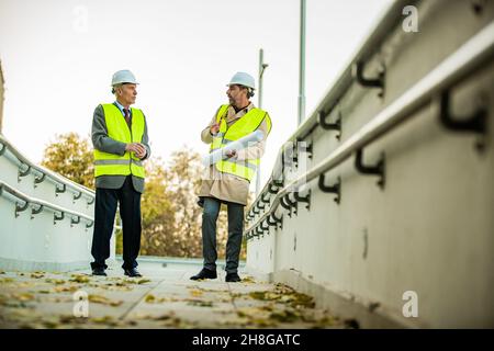 Two senior construction managers are standing and having a conversation about the plans and ideas Stock Photo