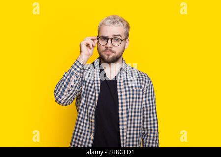 Portrait of a concentrated bearded man in eyeglasses looking at camera isolated over yellow background. Stock Photo