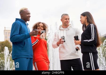 Group of young people of different nationalities in sportswear are drinking coffee and chatting. Two men and two women. Healthy lifestyle. There is a Stock Photo