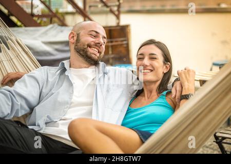 young couple lying on hammock, people relaxing on vacation, happy couple hugging and having a rest on a terrace on sunset Stock Photo