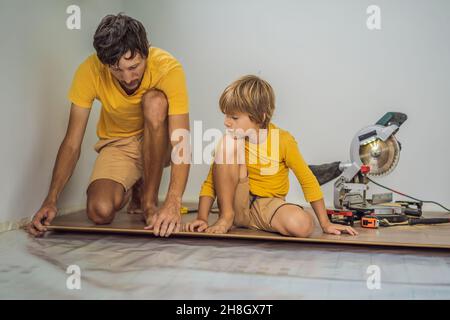 Father and son installing new wooden laminate flooring on a warm film floor. Infrared floor heating system under laminate floor Stock Photo