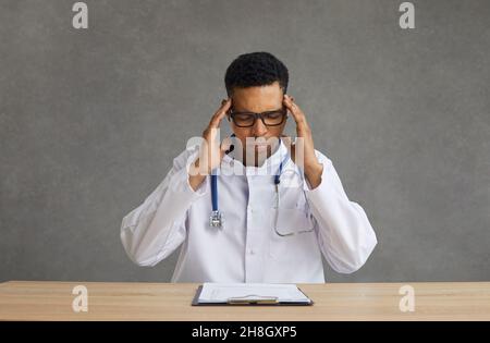 Young african american male doctor suffering from headache sitting at desk Stock Photo