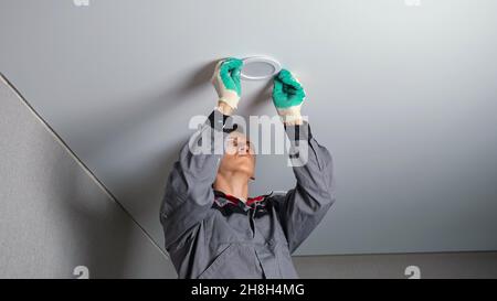 Electrician installs light on ceiling at flat renovation Stock Photo