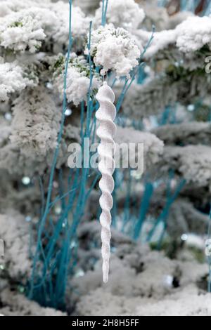 Icicle shaped white, glittery bauble hanging on a  snow-covered Christmas tree Stock Photo