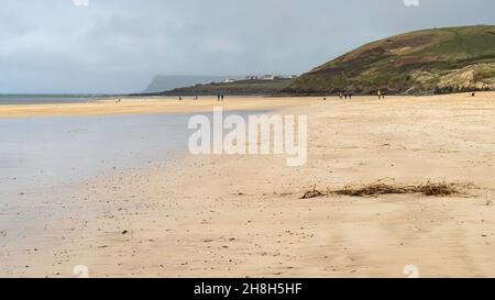 People and dogs strolling on a sandy bay in North Cornwall on a breezy November day lit by a shaft of sunlight. Stock Photo