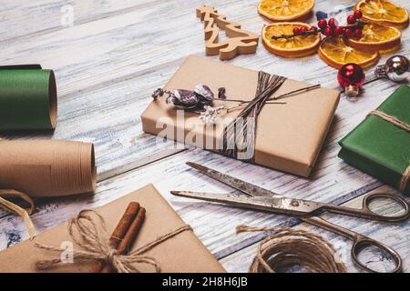 Preparing gift boxes for Christmas. Decoration and wrapped christmas presents on wooden table. Wrapping paper, scissors and holiday ornaments Stock Photo