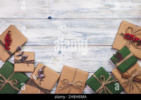 Wrapped Christmas presents with decoration on white wooden table. Flat lay of gift boxes in green and brown kraft wrapping paper Stock Photo
