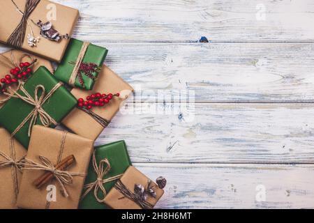 Wrapped Christmas presents with decoration on white wooden table. Flat lay of gift boxes in green and brown kraft wrapping paper Stock Photo