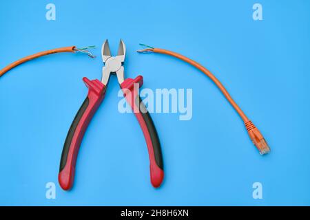 Cutting a computer network wire with wire cutters, blue studio background Stock Photo