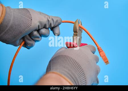 Cutting a computer network wire with wire cutters, blue studio background Stock Photo