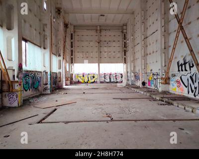 Large abandoned empty warehouse interior. Signatures on the wall using colorful spray paints. cardboard on the floor. Interior of the warehouse with white walls. Factory room. Empty loft. Stock Photo