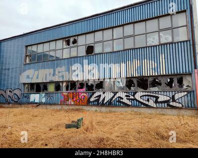 Large warehouse with glass windows being shot with a shotgun. Abandoned warehouse with wall chalking. Rows of glass windows. Damaged windows.  Stock Photo