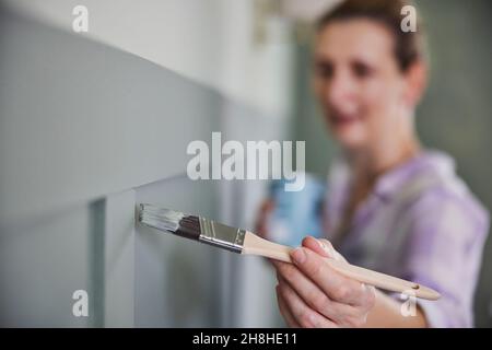 Woman Painting Wall With Panelling In Room Of House With Paint Brush Stock Photo