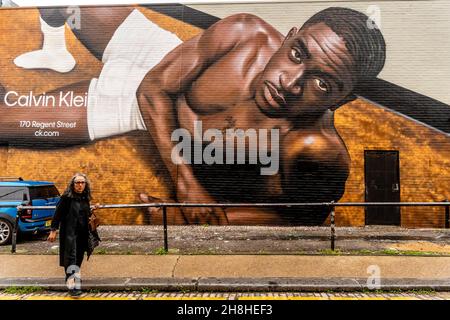 An Afro-Caribbean Woman Walks Past Some Street Art/Graffiti, Shoreditch, London, UK. Stock Photo