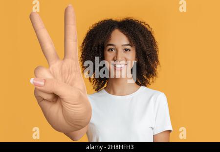 Cheerful mixed race young lady showing peace gesture Stock Photo