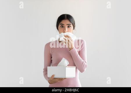 Shocked upset young hindu woman suffering from flu, blows nose, cough, holding box of napkin Stock Photo