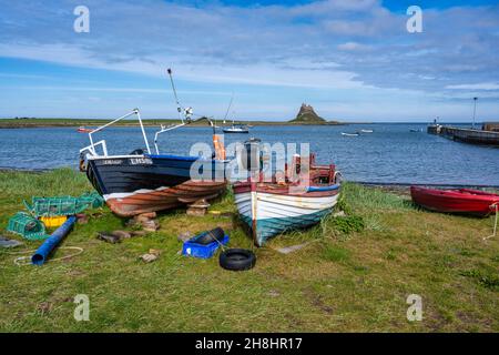 Fishing boats drawn up on beach with distant view of Lindisfarne Castle on Holy Island on the Northumberland Coast of England, UK Stock Photo