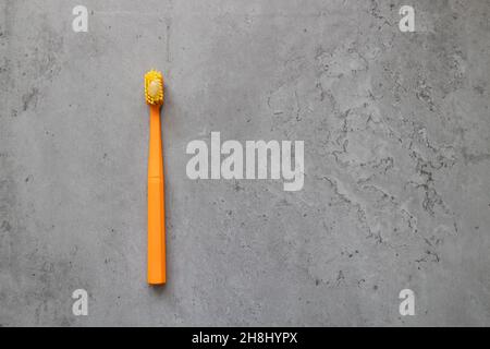 Orange plastic toothbrush with toothpaste on gray concrete table. Dental health at home. Stock Photo