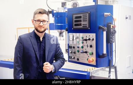 Worker man entering data in CNC drill machine at automatic factory floor. Modern process metal detail production. Stock Photo